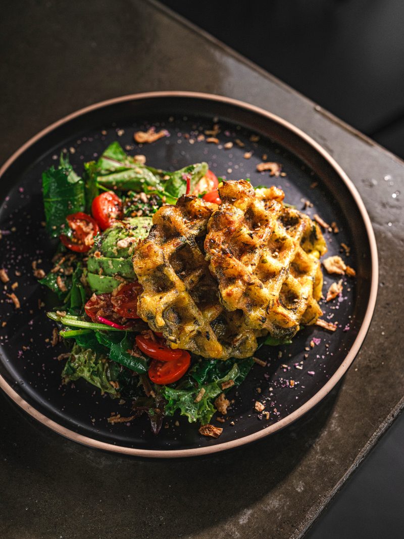 A savoury waffle plated with greens and tomato for brunch