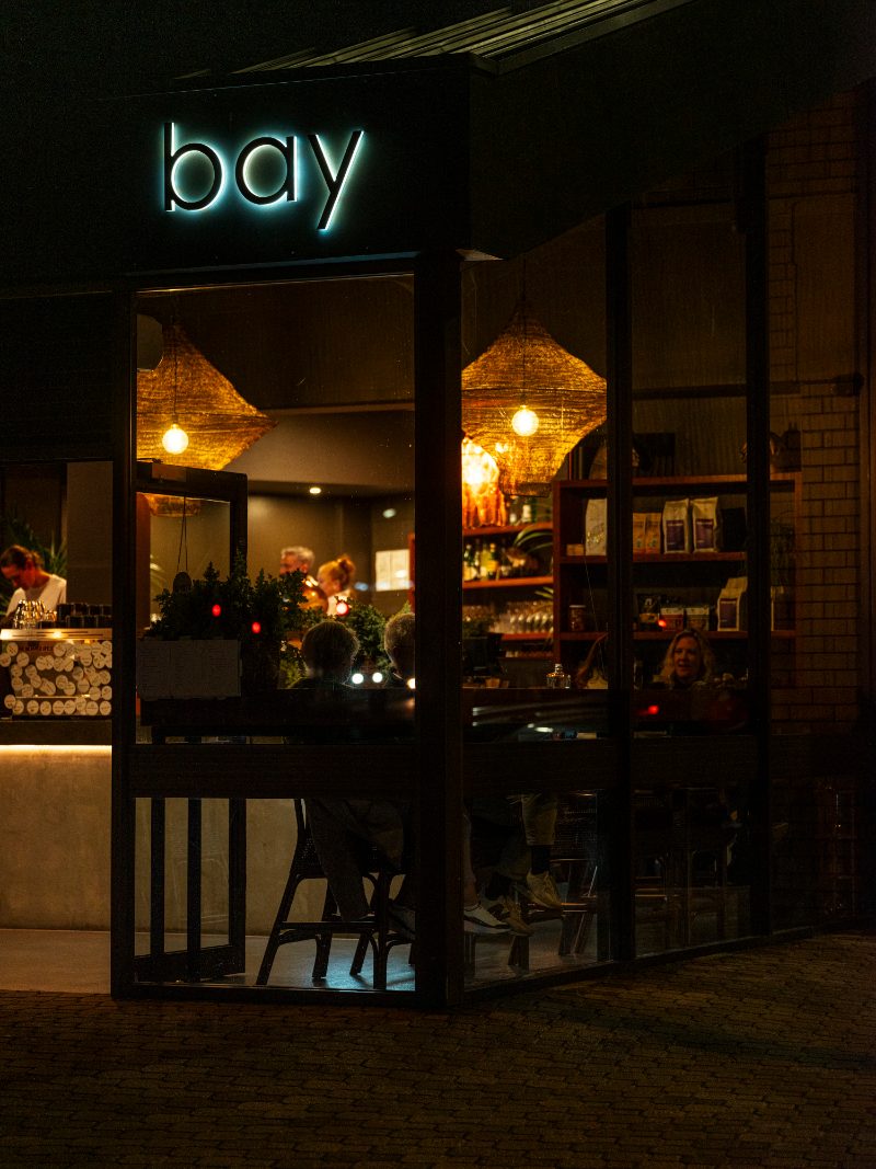 The lit Bay Bellerive shopfront at night, seen from the street